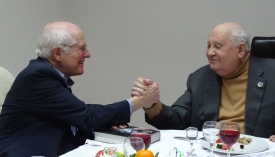 Photo of the author clasping right hands with Mikhail Gorbachev while both are seated at lunch table. Author's left hand rests on a copy of his biography of Gorbachev.